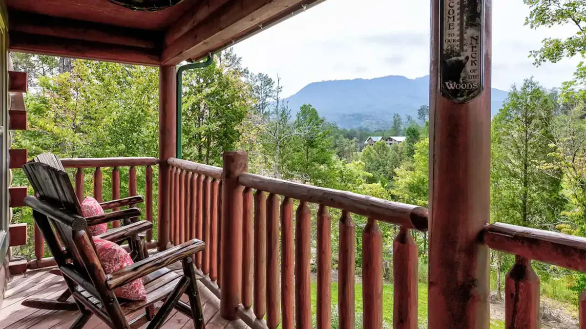 This image showcases a peaceful porch scene with classic wooden rocking chairs facing a sweeping mountain view. Greenery surrounds the porch, creating a tranquil setting ideal for morning coffee or evening relaxation. The porch is bathed in natural light, with ample space for guests to enjoy the outdoors comfortably.