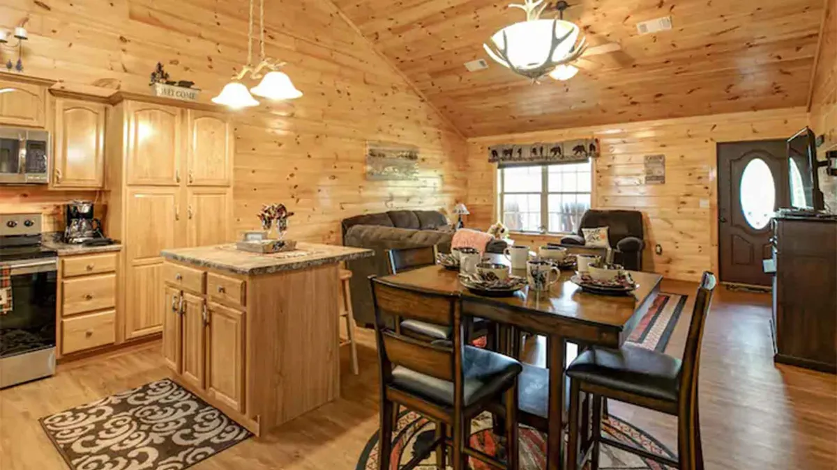 This angle focuses on the open-concept kitchen and dining space, featuring wooden kitchen cabinets, a kitchen island, a dining table set for a meal, and a comfortable seating area. The layout emphasizes togetherness, with spaces seamlessly connecting for family meals and celebrations.