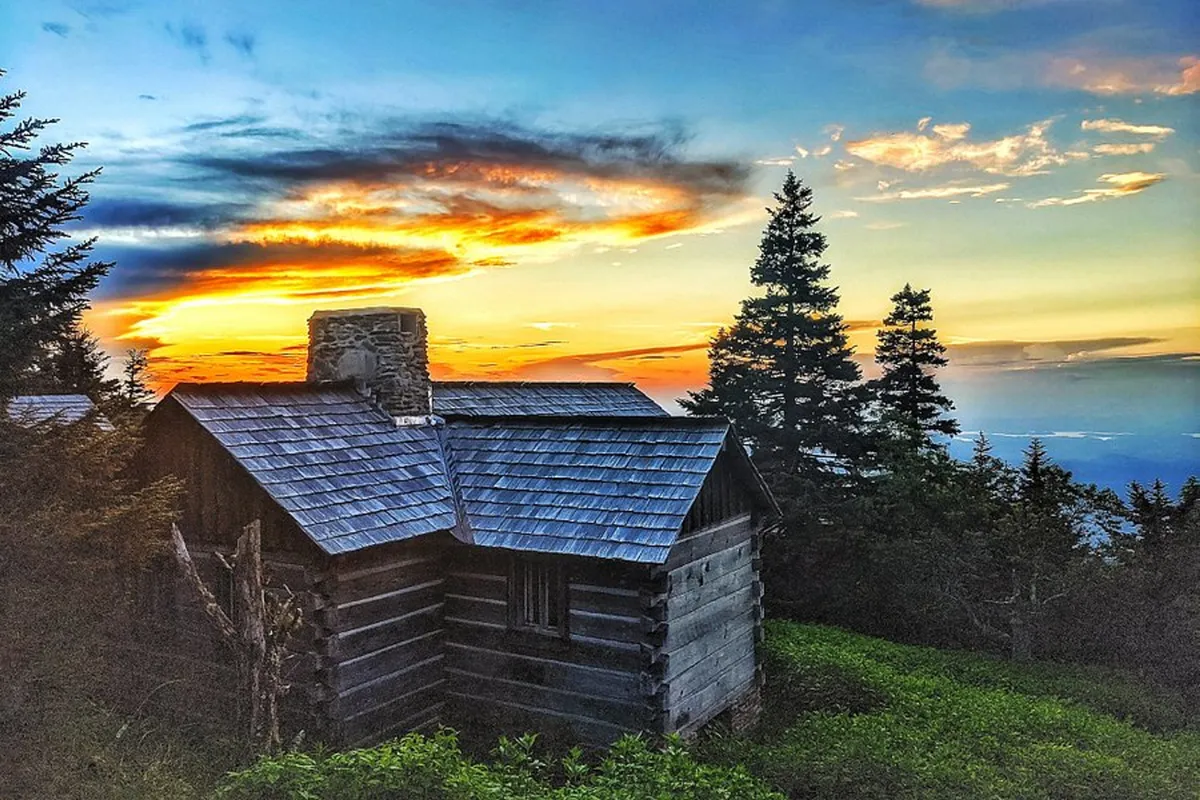 An inviting exterior shot of a rustic cabin set against the backdrop of a colorful sunset and surrounded by trees. The image conveys a sense of peaceful retreat, perfect for relaxing evenings with s'mores, stories, and family bonding after a day of local adventures.