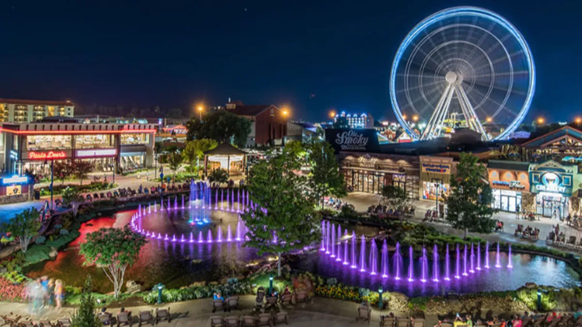 This vibrant exterior image captures The Island in Pigeon Forge, with its iconic ferris wheel, illuminated fountain, lively shops, and seating areas. The scene is bustling with energy, hinting at the many family-friendly activities, dining options, and entertainment possibilities nearby.