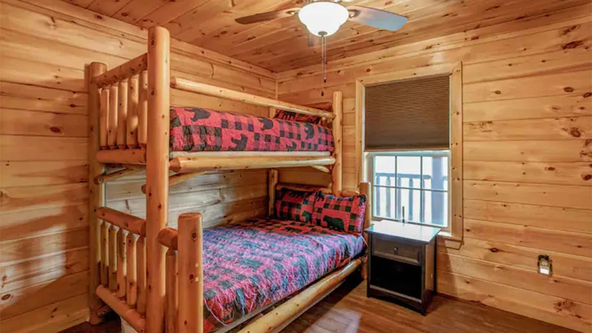 A welcoming bedroom with built-in bunk beds, wooden walls, a window letting in early morning sunlight, and a nightstand. The space radiates warmth and is clearly designed for kids or groups, perfect for sleepovers and family bonding.